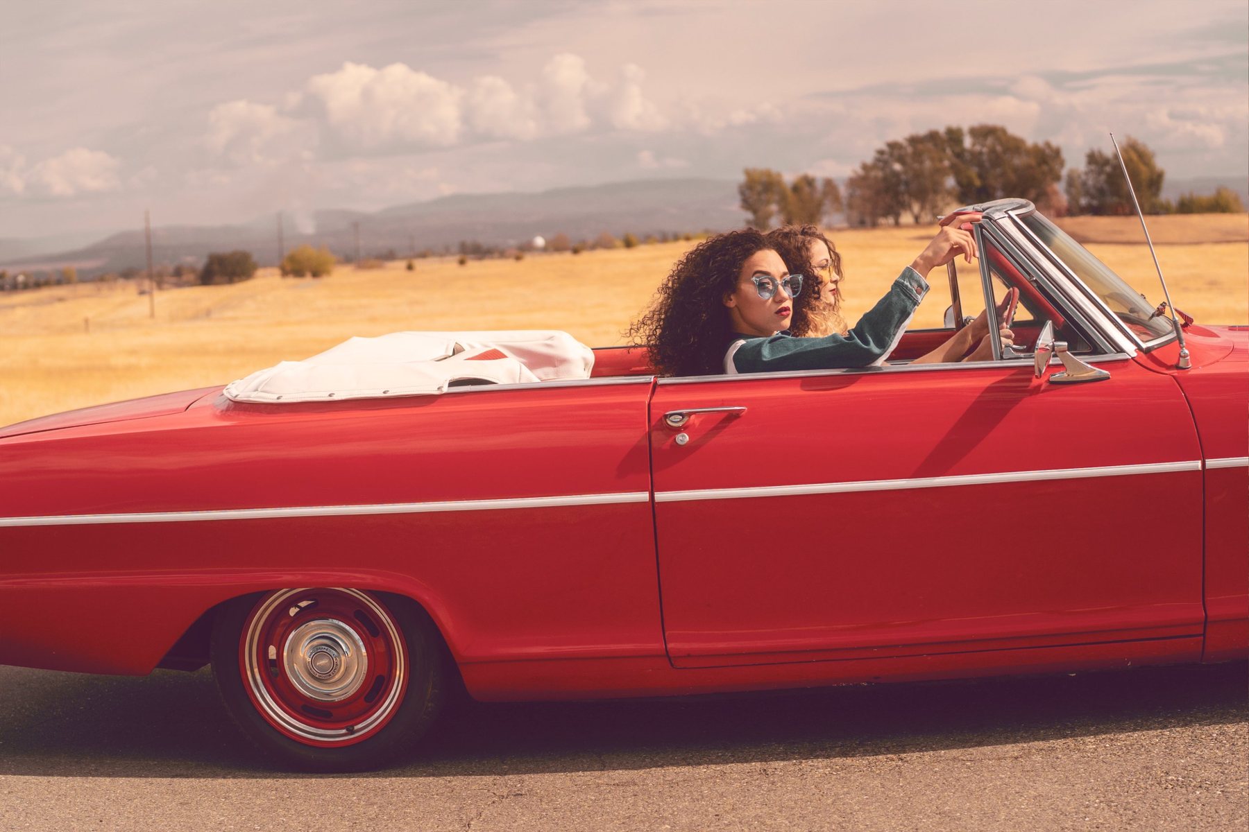 Two women in a red convertible on a country road